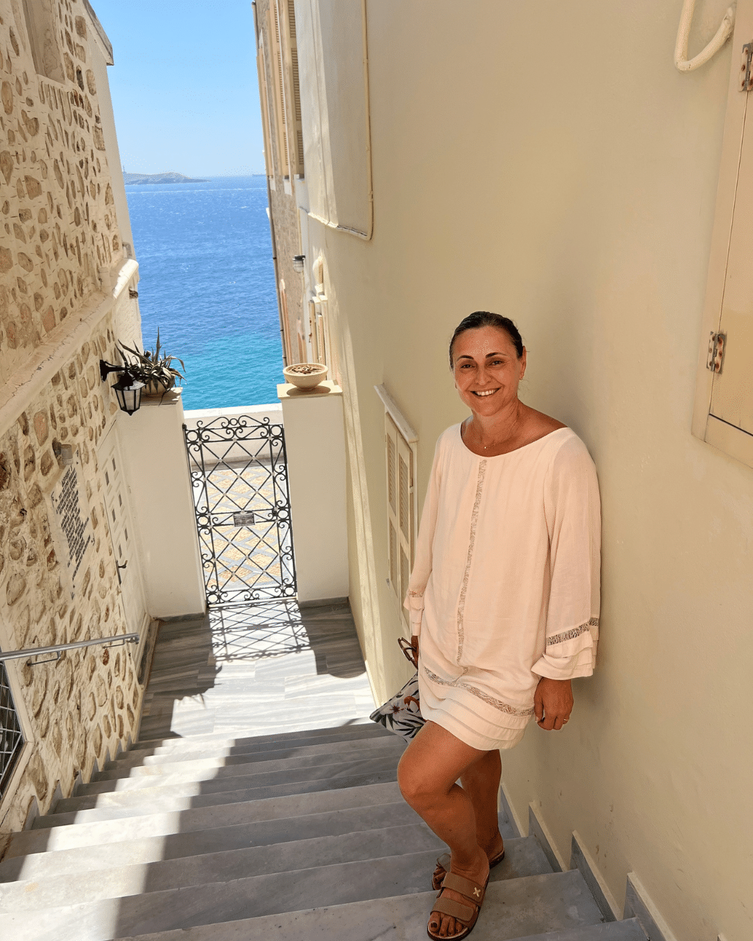 Summer Style in Greece | Style Culture Kerry wearing a lightweight white summer dress on the Greek Islands, with the Aegean Sea in the background.